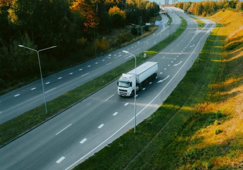 A top view of a truck driving along a highway road in evening time under a sunny blue sky
